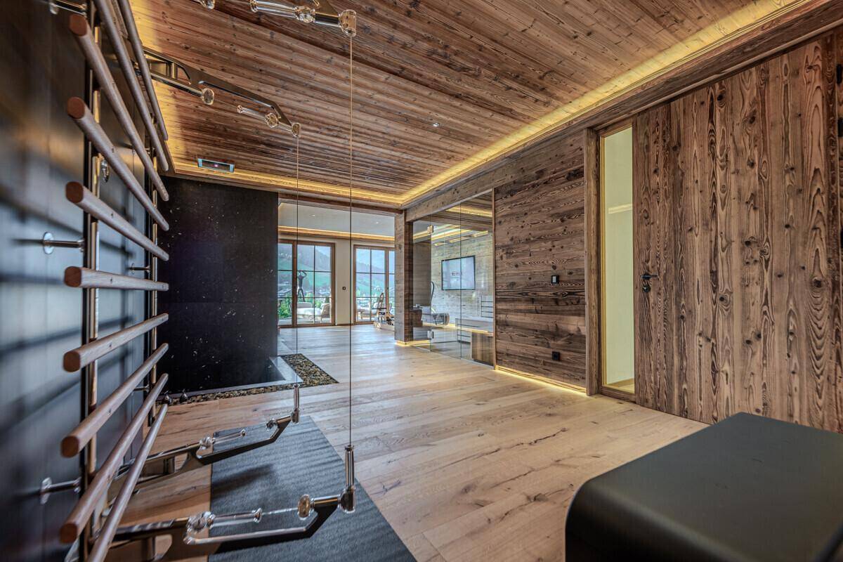 Moderner Fitnessraum mit Holzwänden, Sprossenwand und Blick auf die umliegende Landschaft.