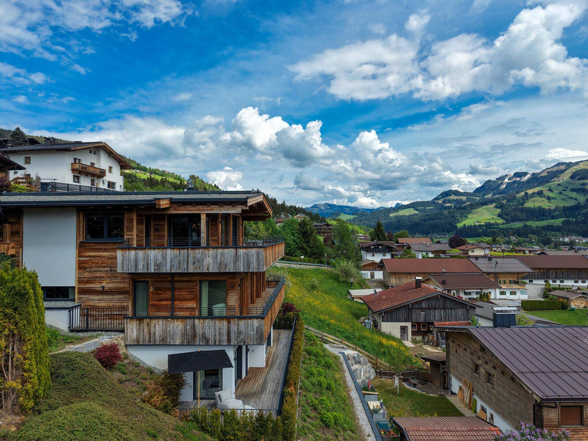Panoramablick auf das moderne Chalet und die umliegende Berglandschaft mit Dorf.