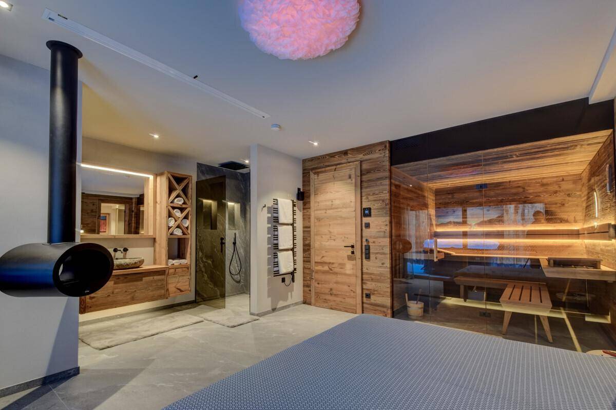Modernes Schlafzimmer mit integriertem Badbereich, freistehendem Kamin und privater Sauna, gestaltet mit warmen Holzelementen.