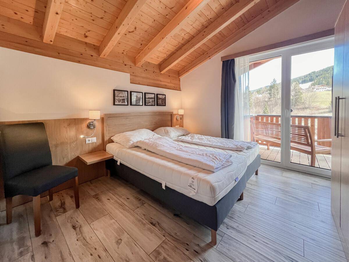 Gemütliches Schlafzimmer mit Holzbalkendecke, Doppelbett und Zugang zu einem sonnigen Balkon.