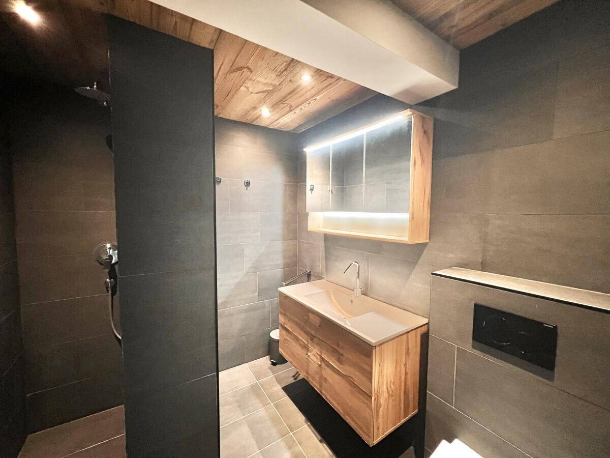 Modernes Badezimmer mit dunklen Fliesen, Holzwaschtisch und begehbarer Dusche.