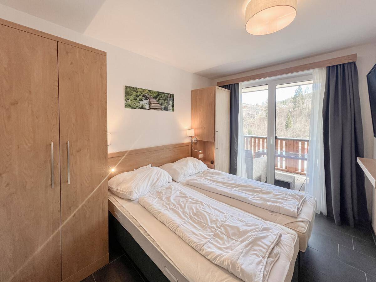Helles Schlafzimmer mit Doppelbett, großem Holzschrank und Zugang zu einem sonnigen Balkon.