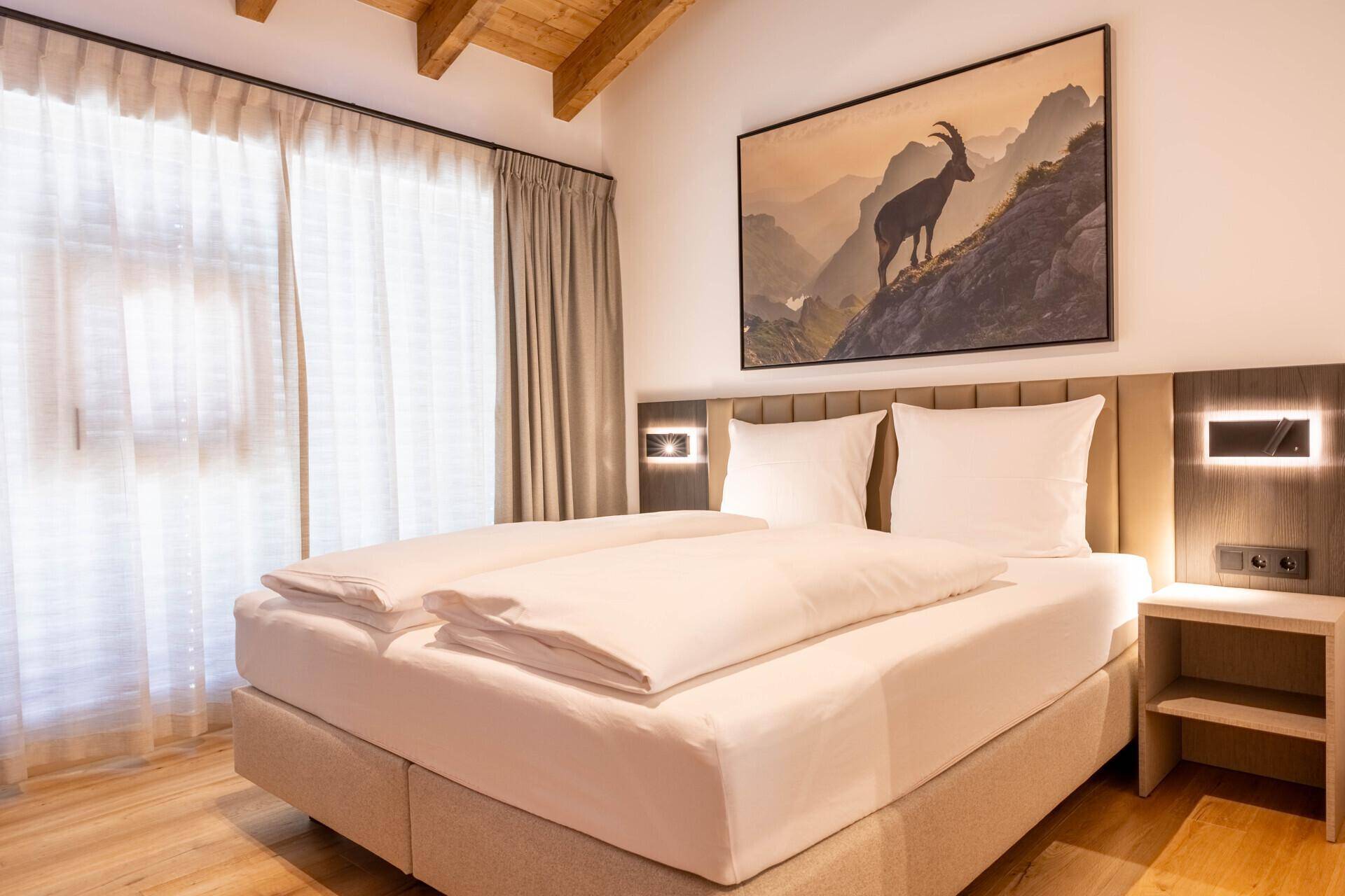 Gemütliches Schlafzimmer mit Doppelbett, Holzboden und Bergbild an der Wand.