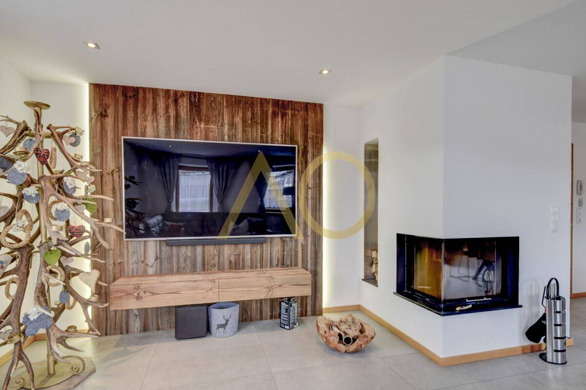 Gemütliches Wohnzimmer mit modernem Kamin, Holzwand und großem Fernseher.