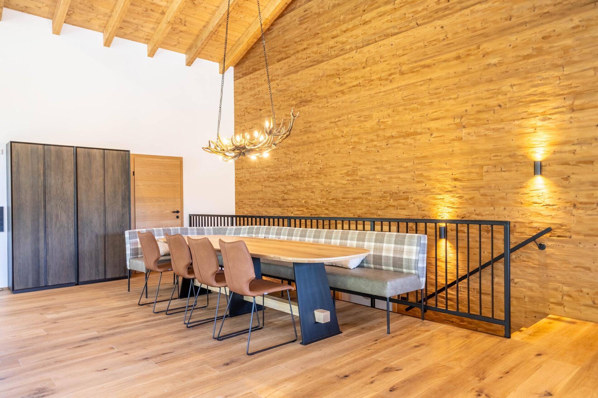 Geräumiger Essbereich mit Holztisch, Sitzbank und Hirschgeweih-Lampe in rustikalem Stil.