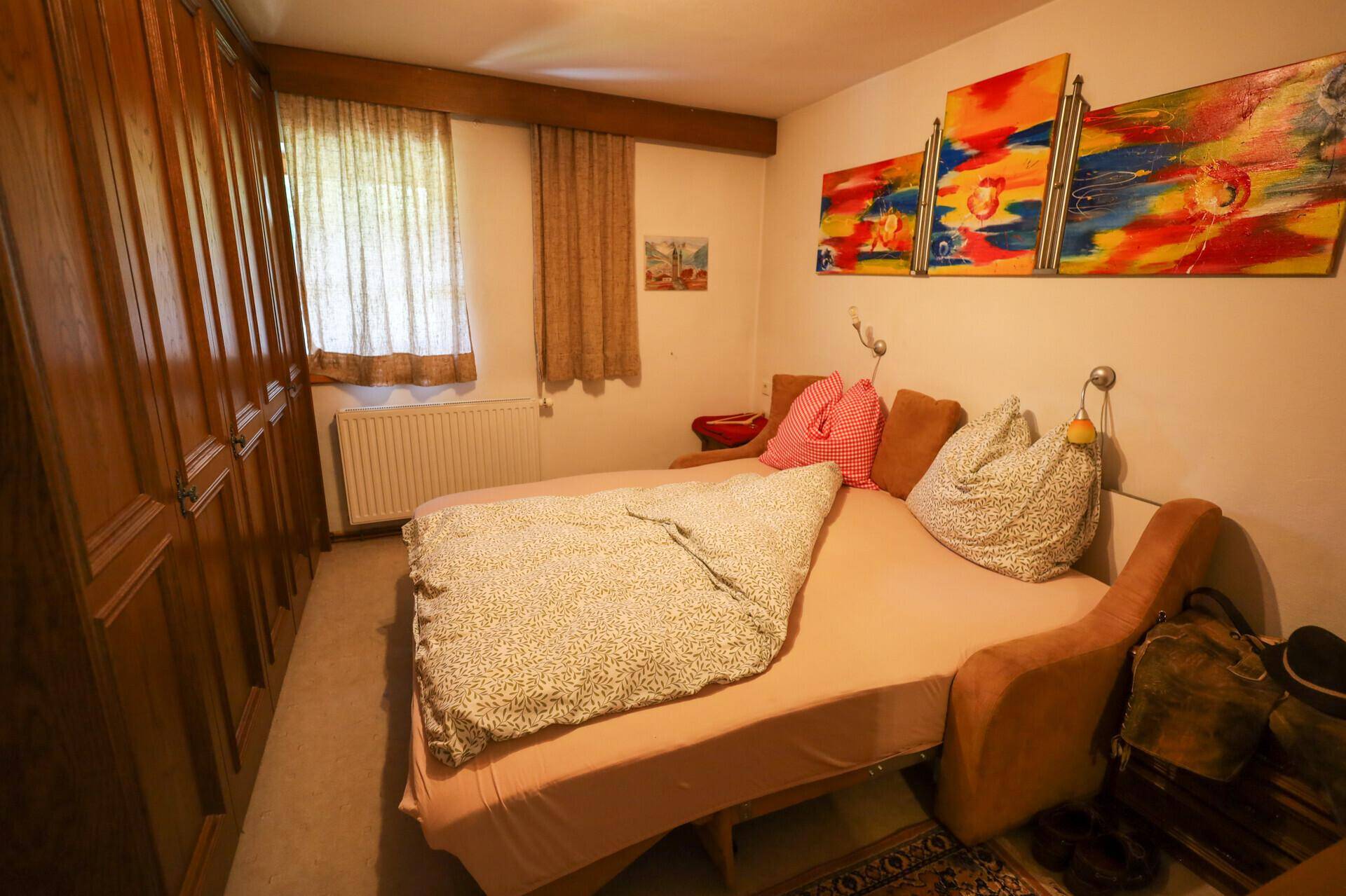 Gemütliches Schlafzimmer mit Holzkleiderschrank, Doppelbett und farbenfroher Wandkunst.