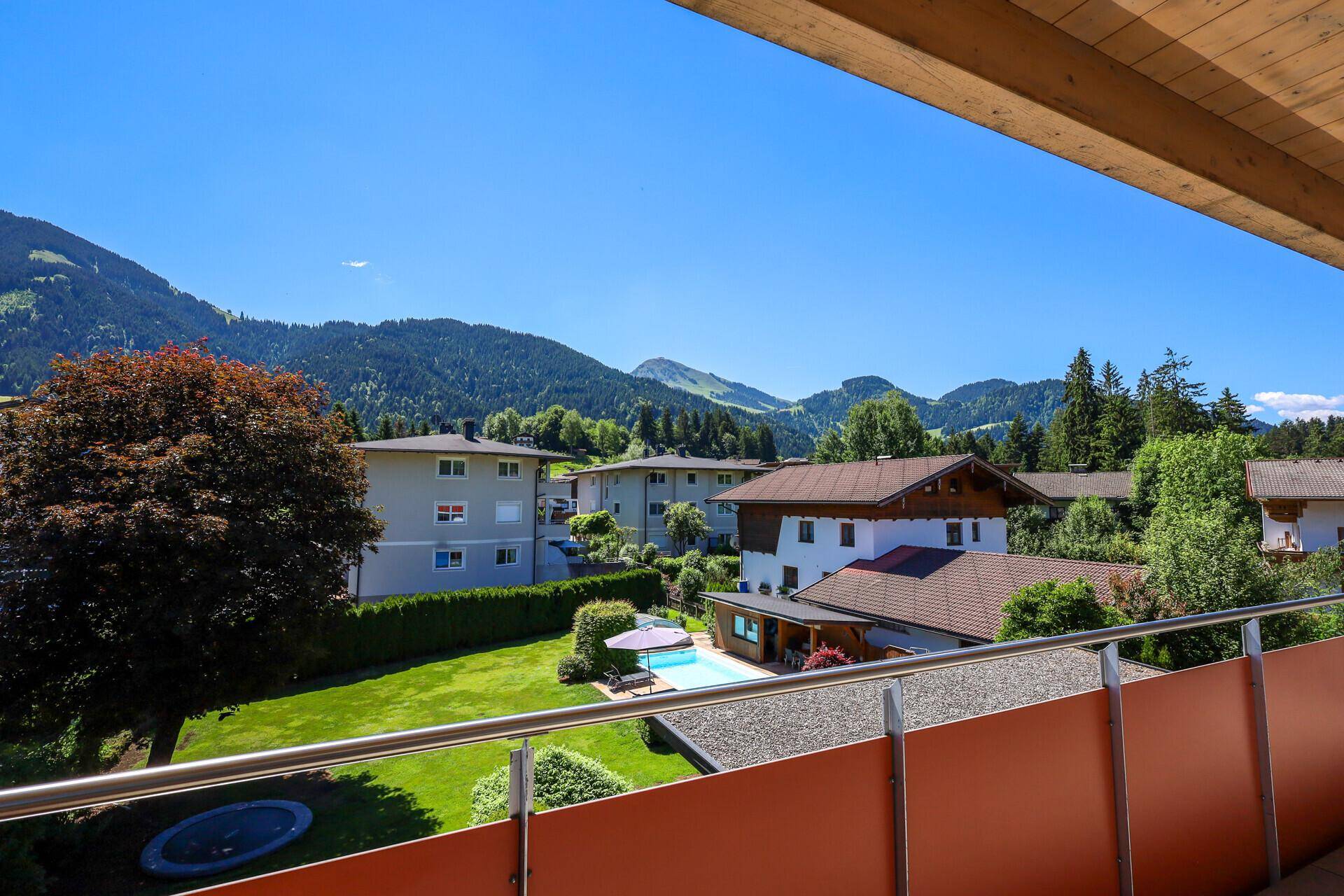 Balkon mit weitem Blick über die grüne Landschaft, Häuser und Berge unter blauem Himmel.