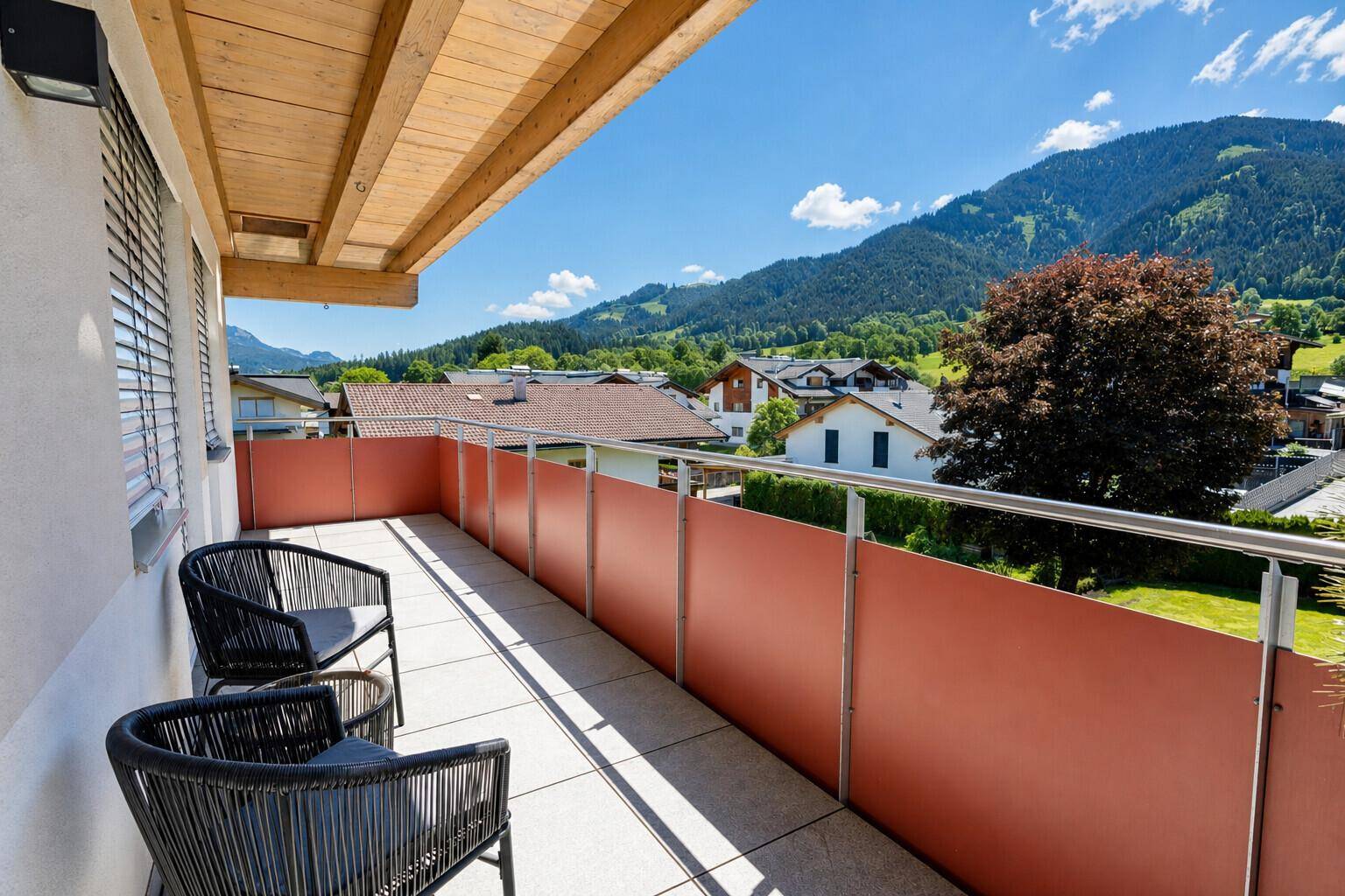 Langer Balkon mit modernen Sitzgelegenheiten und Panoramablick auf die umliegende Berglandschaft und Häuser.
