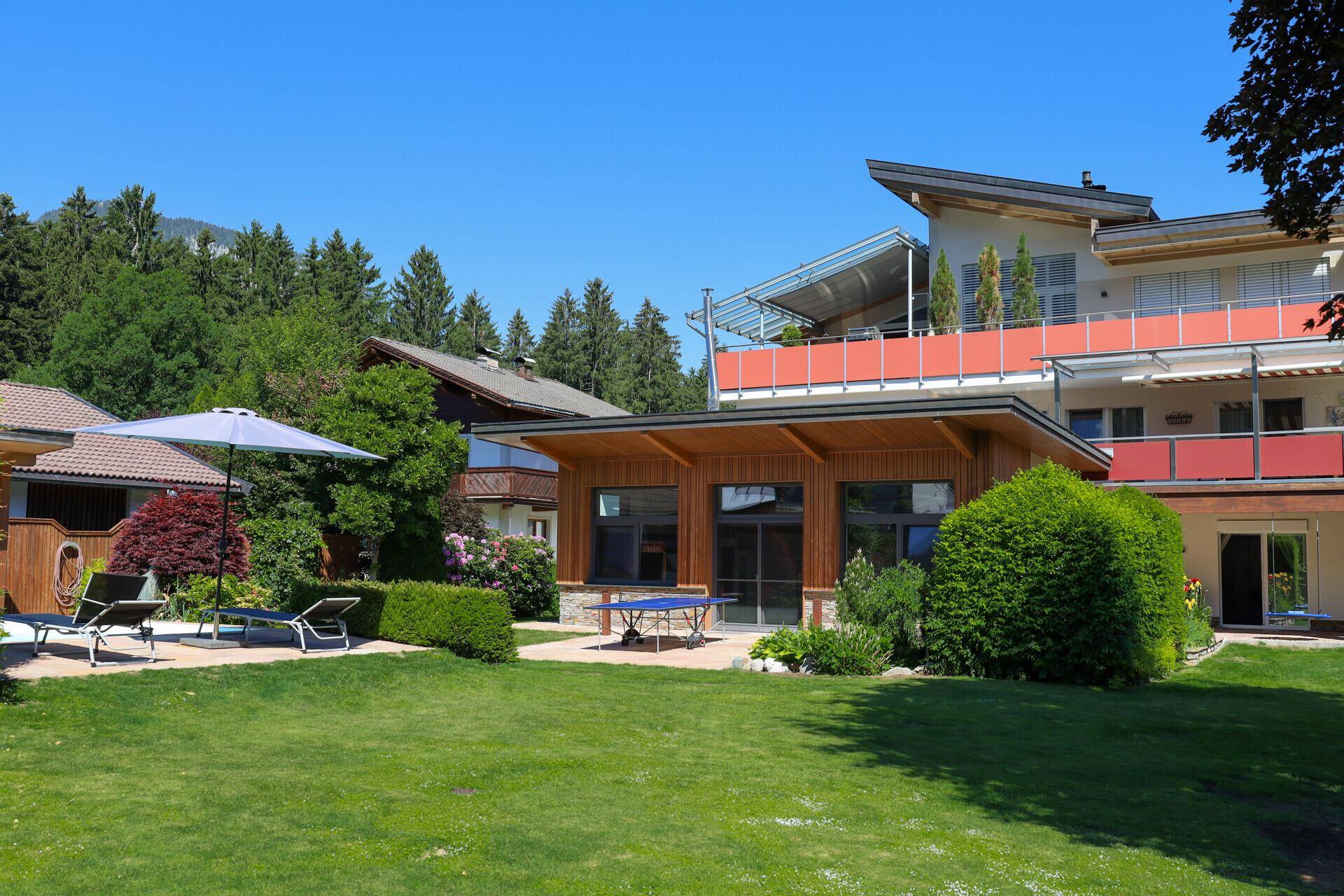 Großer gepflegter Garten mit Rasenfläche, Bäumen und einem modernen Haus im Hintergrund.