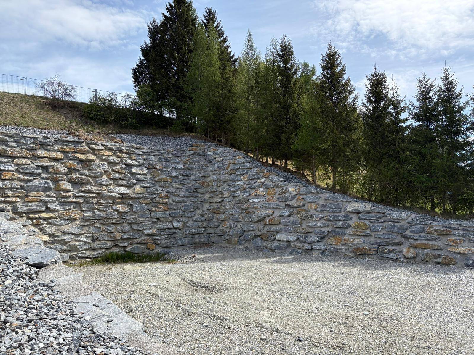 Nahaufnahme der robusten Natursteinmauer, die den Hang sichert, mit Bäumen darüber.