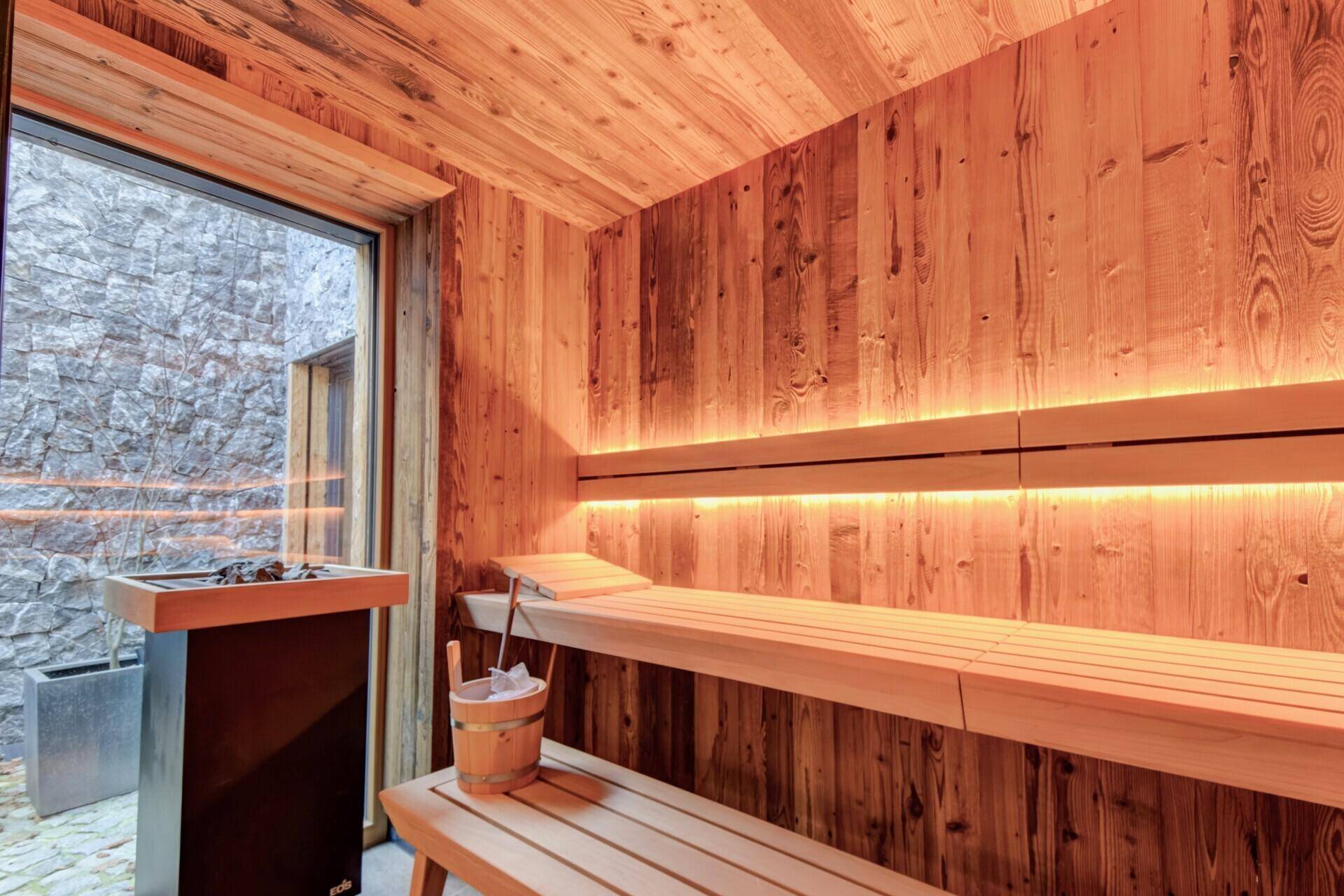 Innenansicht der Sauna mit Holzbänken, Ofen und Blick nach draußen, hell und einladend.