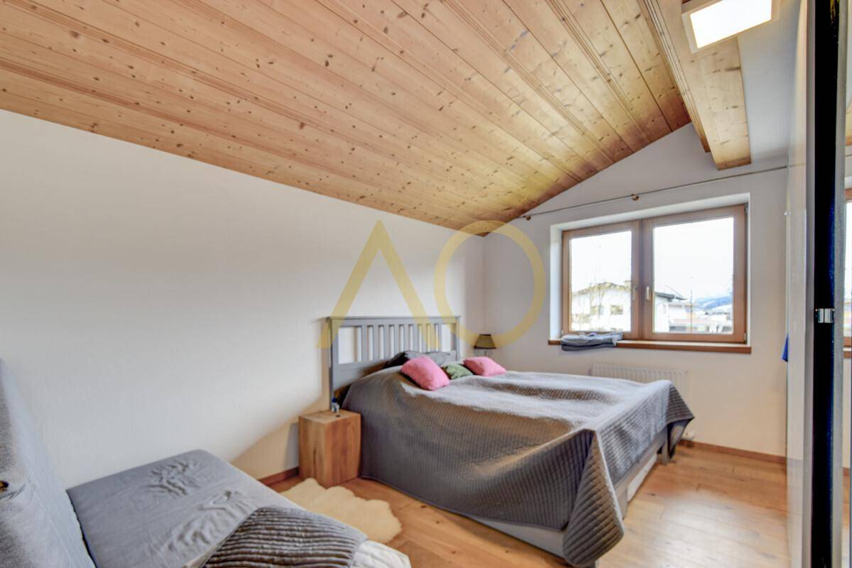 Helles Schlafzimmer im Dachgeschoss mit Holzbalkendecke und großem Fenster.