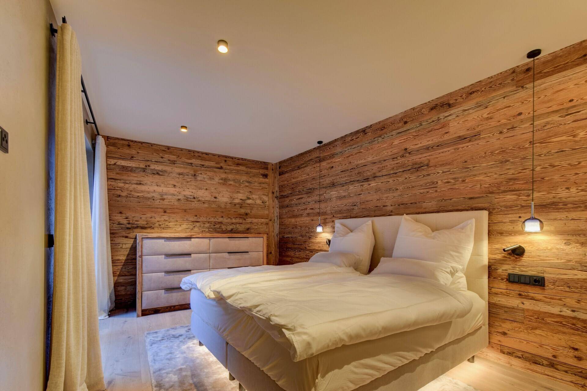 Gemütliches Schlafzimmer mit Holzwand, Bett und Kommode, warm beleuchtet und einladend.