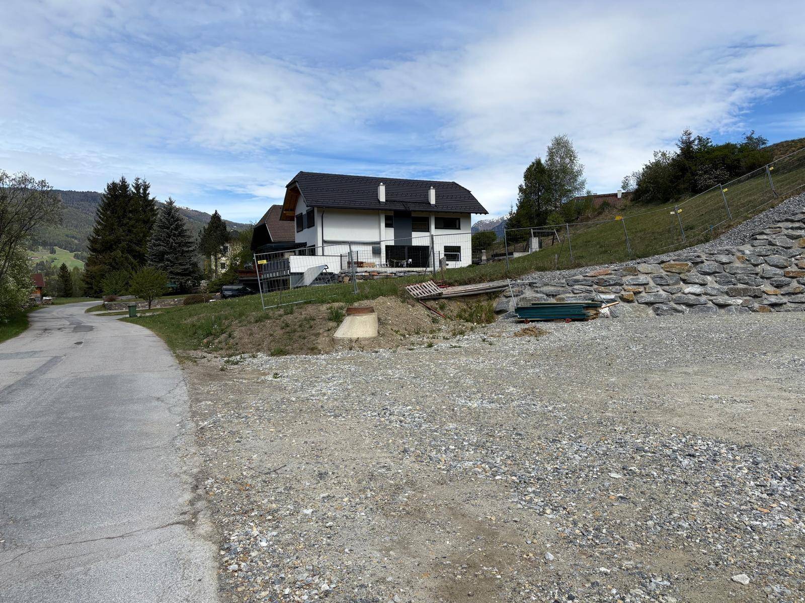 Ansicht des Hauses von der Straße aus, mit Schotterweg und einer Natursteinmauer im Vordergrund.