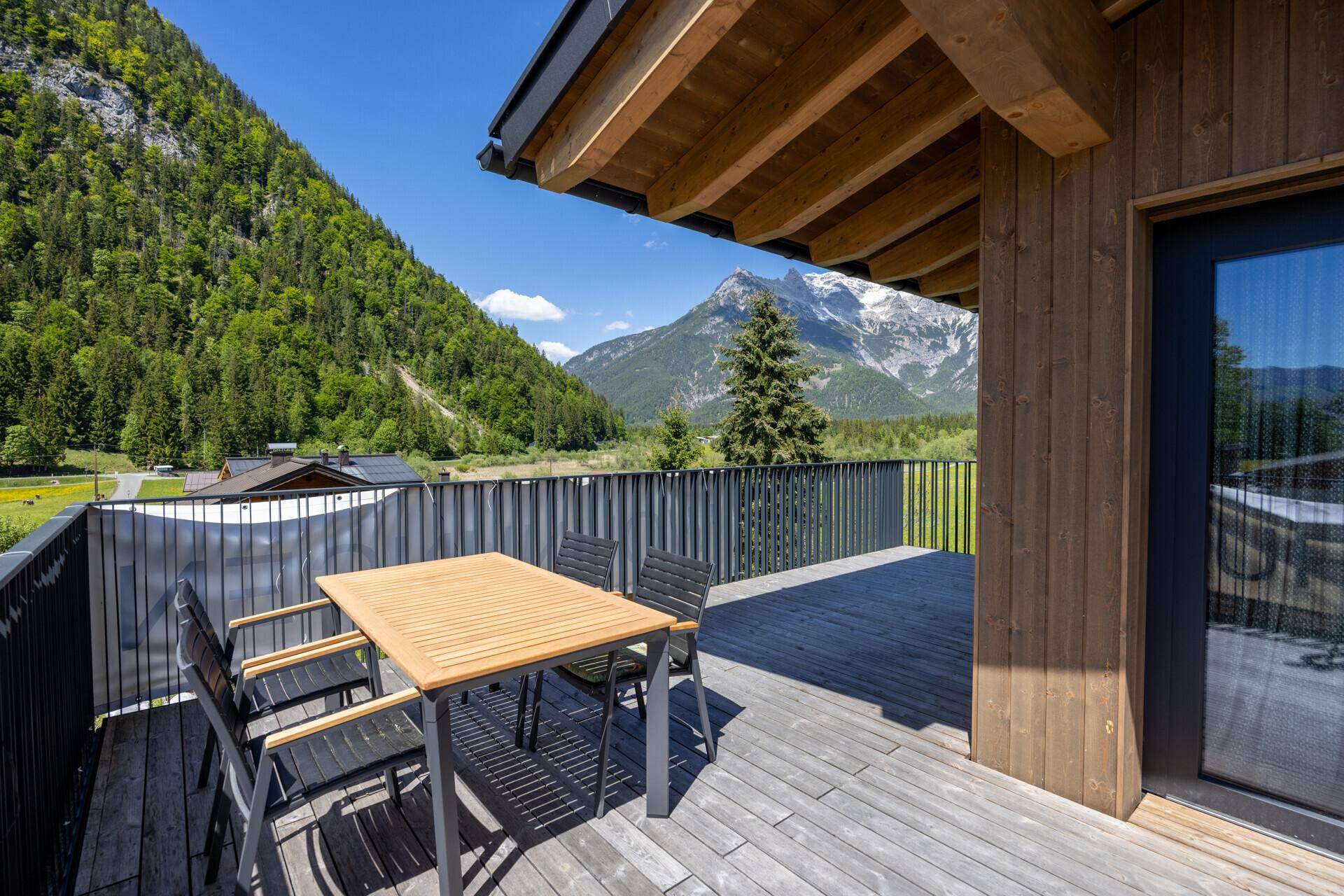 Geräumige Holzterrasse mit Esstisch und Stühlen, umgeben von Bergen und Natur.