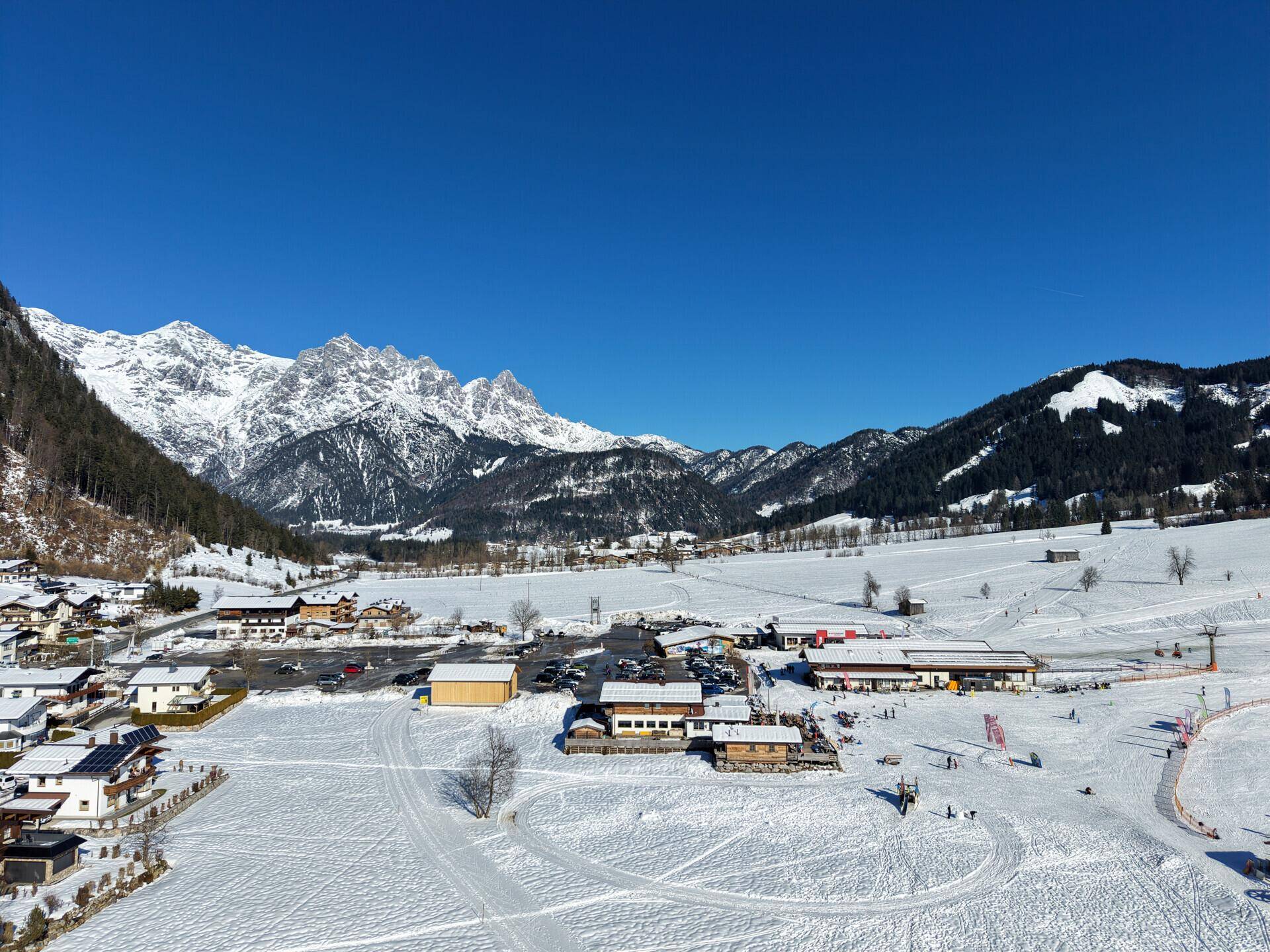 Panoramablick auf ein verschneites Dorf in einem Tal, umgeben von imposanten Bergen.