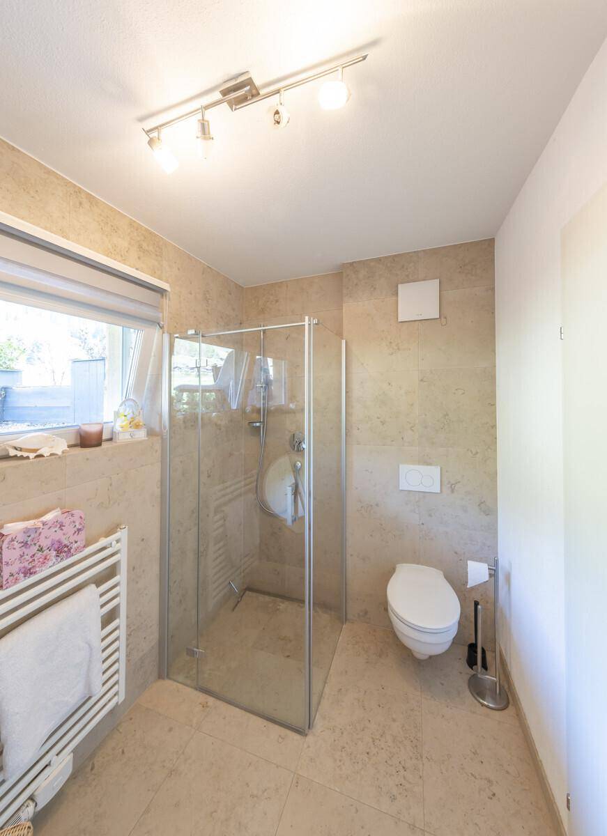 Helles Badezimmer mit begehbarer Dusche, wandhängendem WC und Fenster.