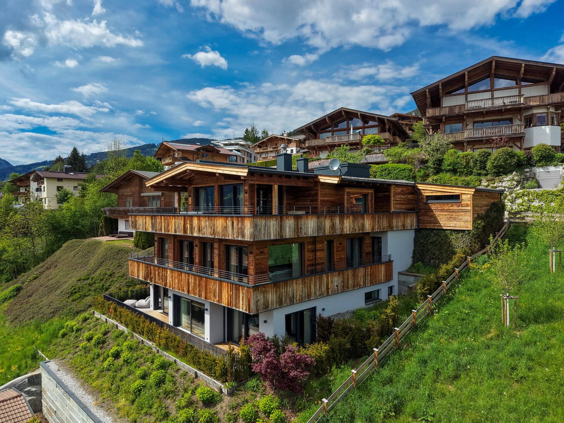 Attraktives Holzchalet mit mehreren Etagen und Terrassen, umgeben von grüner Natur.