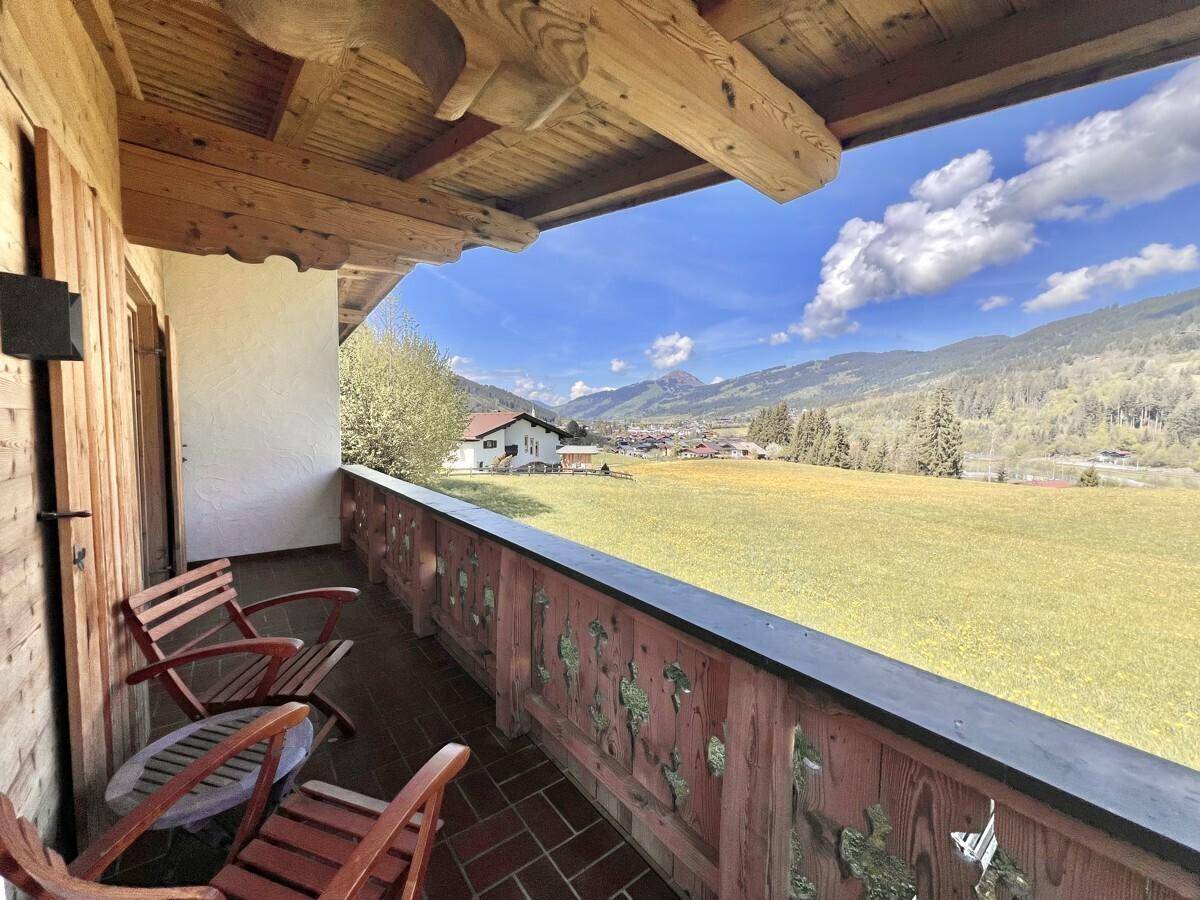 Traditioneller Holzbalkon mit Sitzgelegenheiten und einem weiten Blick auf die Berge und grüne Wiesen.