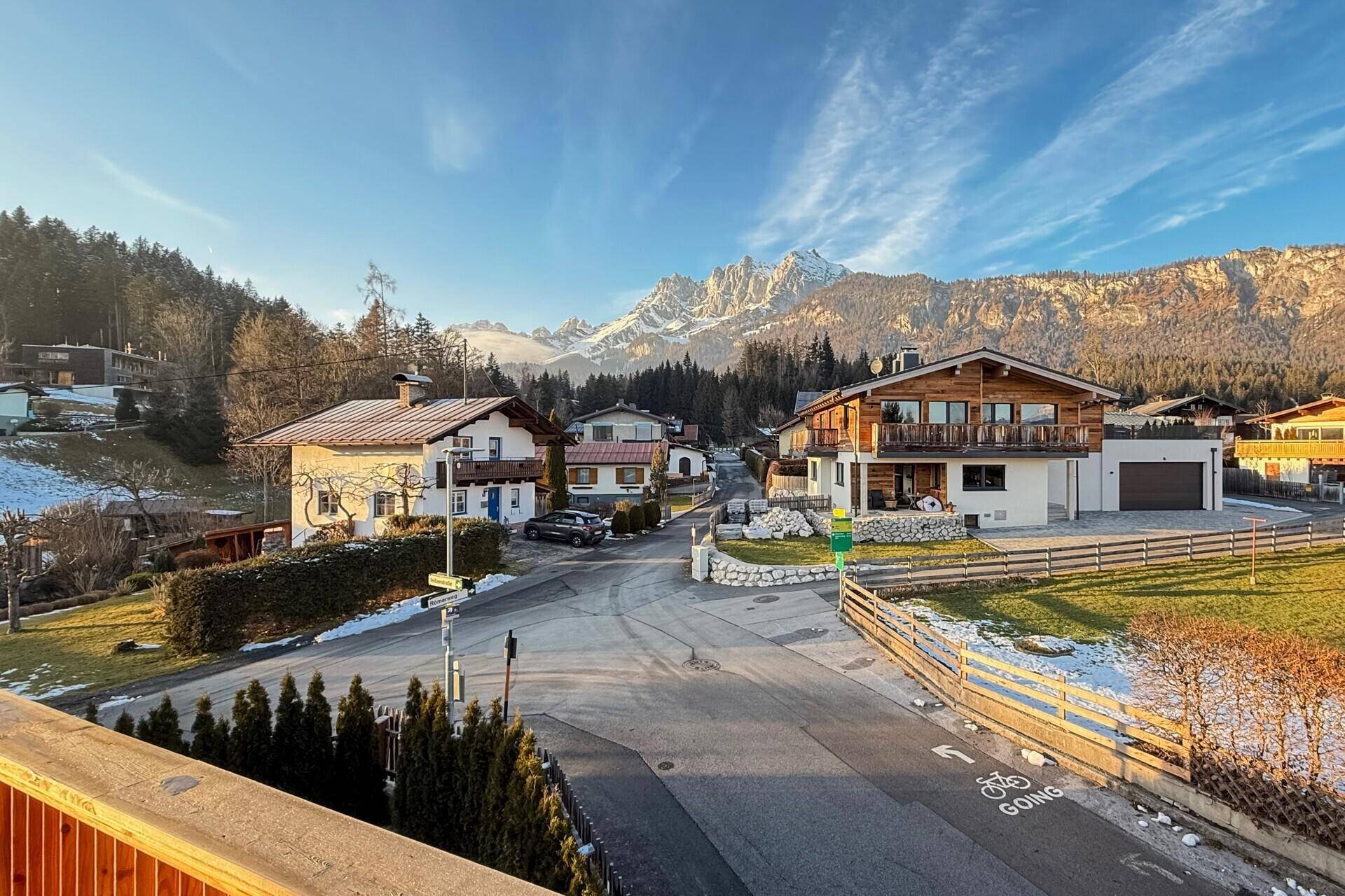 Ruhige Wohnstraße mit Häusern im alpinen Stil und beeindruckender Bergkulisse an einem sonnigen Tag.