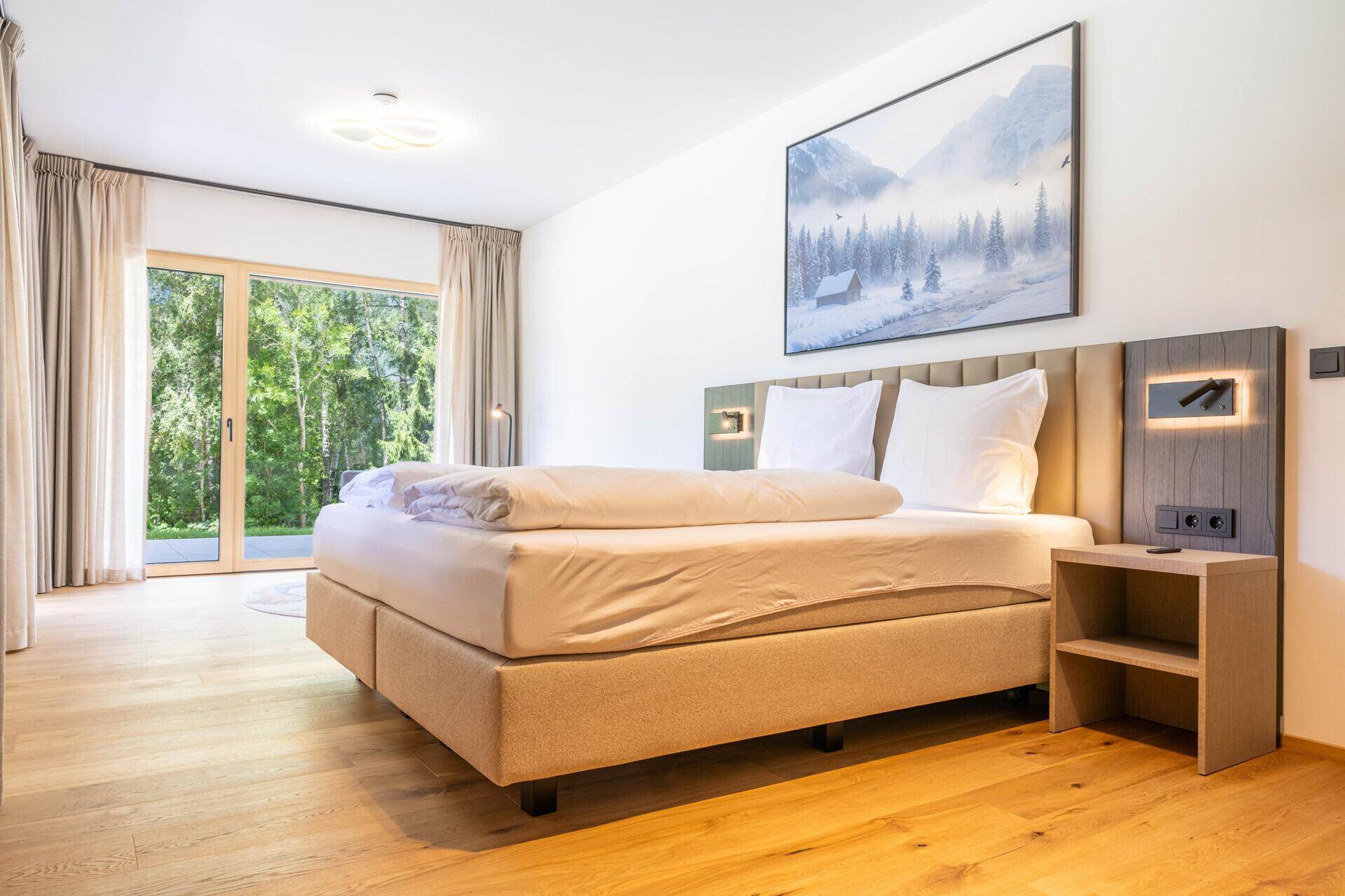 Modernes Schlafzimmer mit Doppelbett, Holzboden und Zugang zu einem Außenbereich.