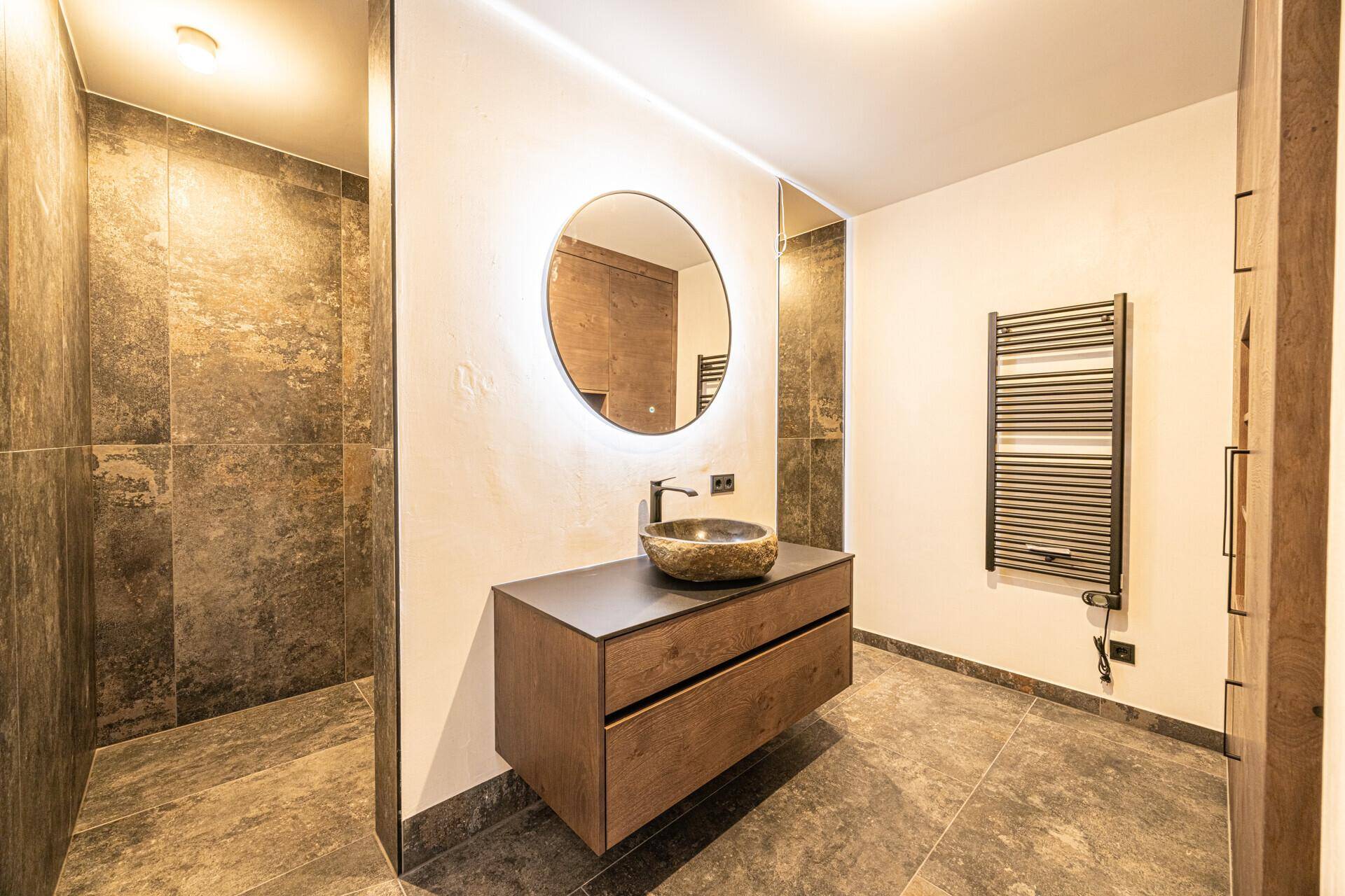 Modernes Badezimmer mit Steinfliesen, schwebendem Waschtisch und beleuchtetem Spiegel.