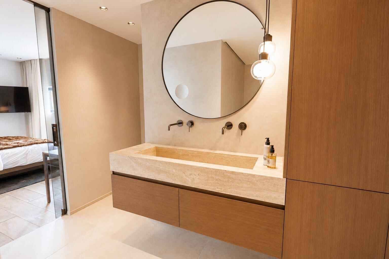 Modernes Badezimmer mit schwebendem Waschtisch aus Naturstein und rundem Spiegel.