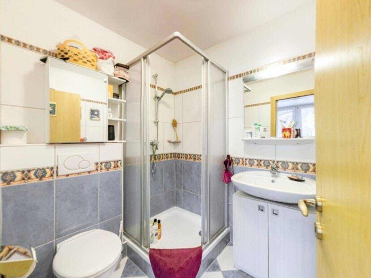 Badezimmer mit Duschkabine, WC und dekorativen blau-weißen Fliesen.