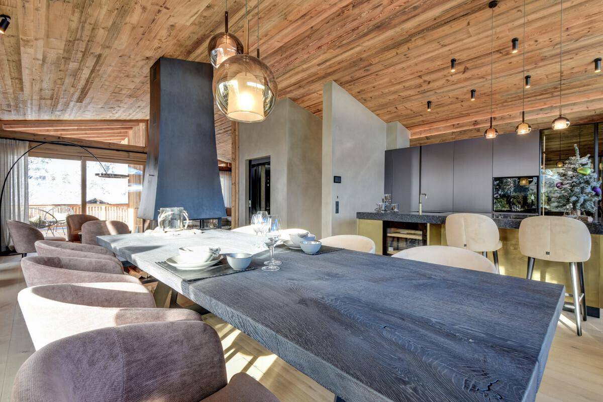 Offener Wohn- und Essbereich mit großem Holztisch, Kamin und moderner Küche im Hintergrund.