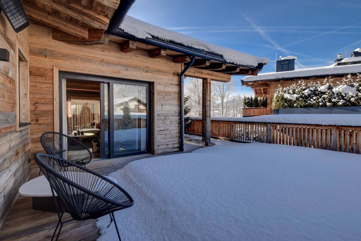 Teilweise überdachte Terrasse mit modernen Outdoor-Sesseln und Blick auf die verschneite Umgebung.