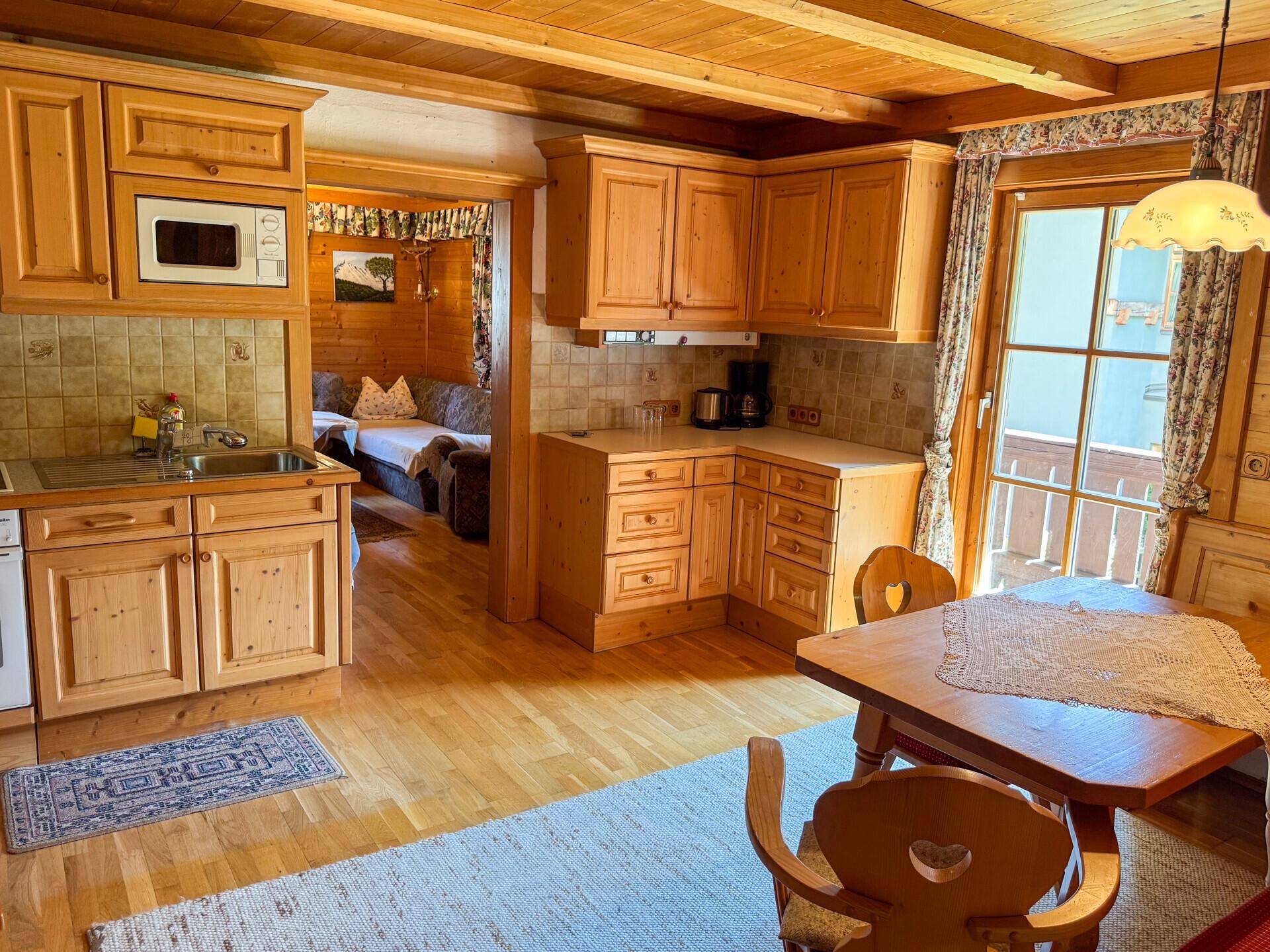 Rustikale Wohnküche mit Holzeinbauten, Esstisch und Zugang zu einem Balkon, alles in Holz gehalten.