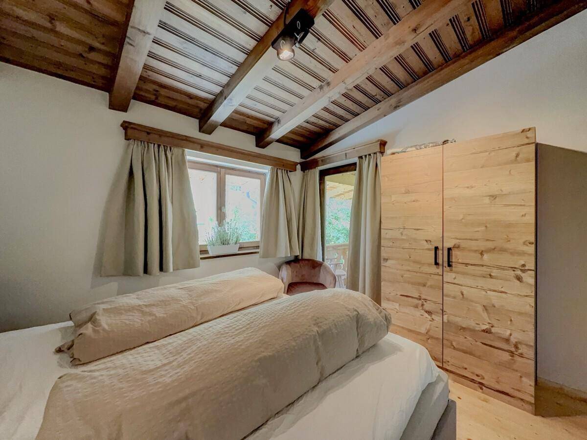 Schlafzimmer mit Holzbalkendecke, Doppelbett und einem großen Holzschrank.