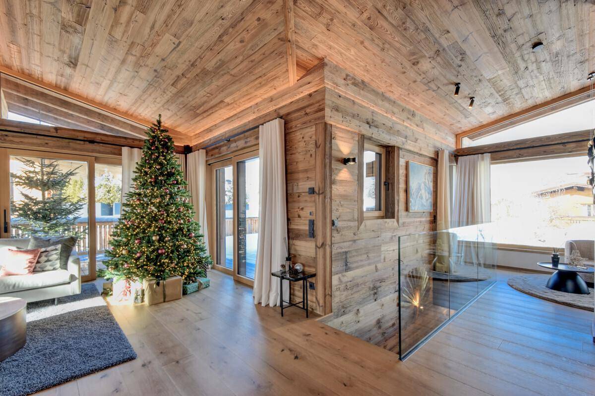 Heller Wohnbereich mit Weihnachtsbaum, Holzwänden und Glasgeländer zur Treppe.