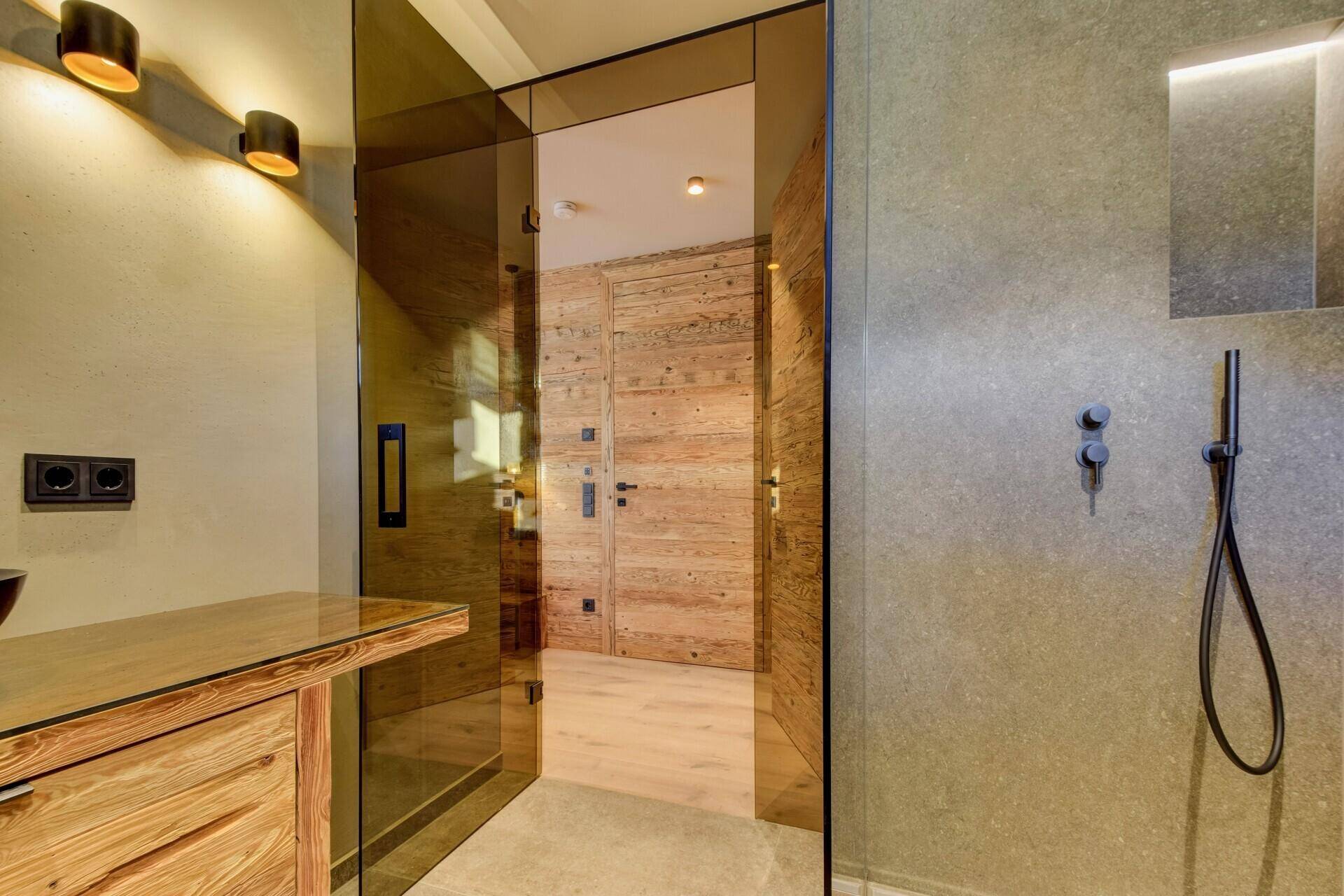 Modernes Badezimmer mit Glasdusche und Holzelementen, offen zum Schlafzimmer hin gestaltet.