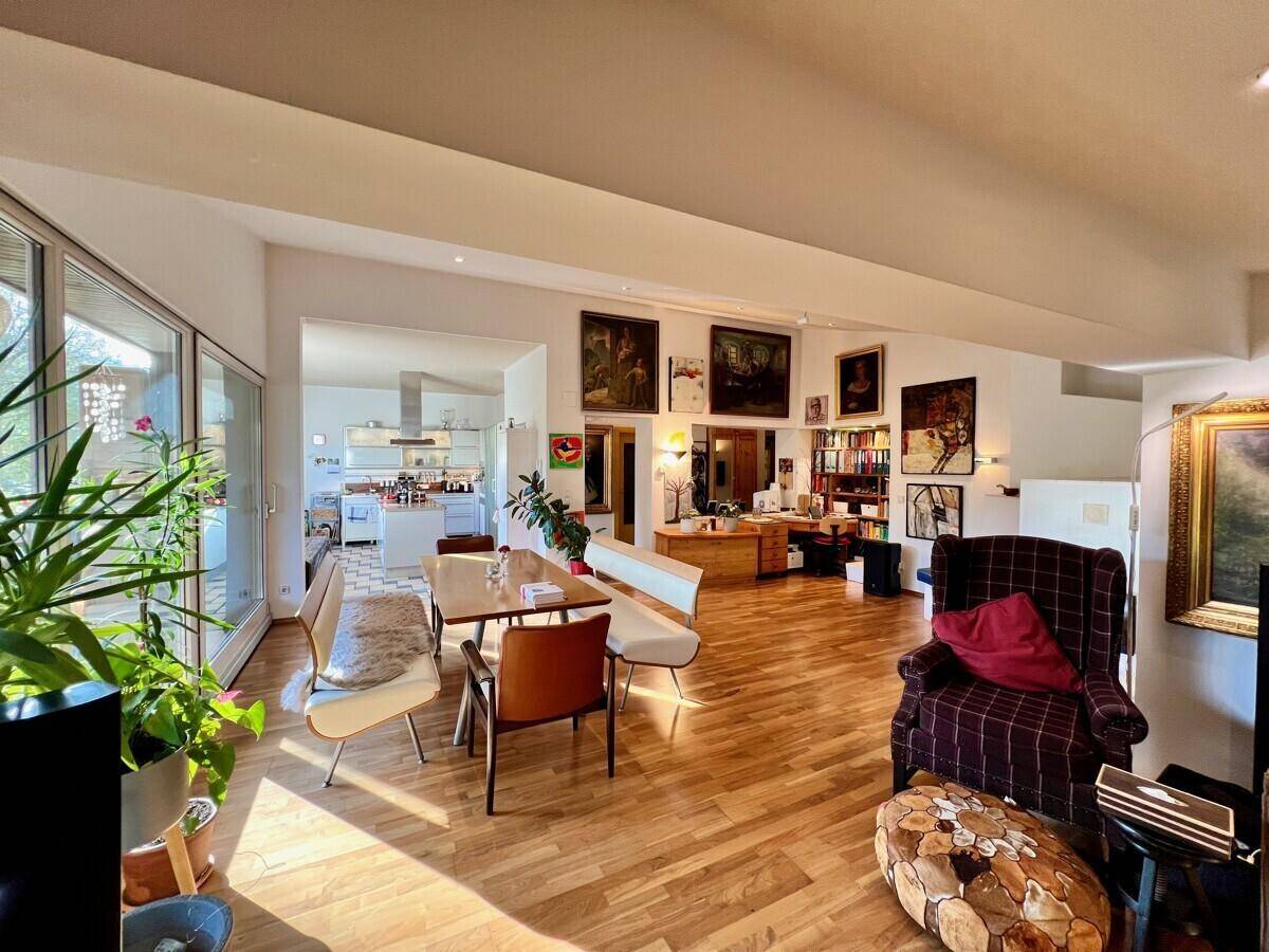 Offener Wohn- und Essbereich mit Holzboden, Kunstwerken und Blick in die moderne Küche.