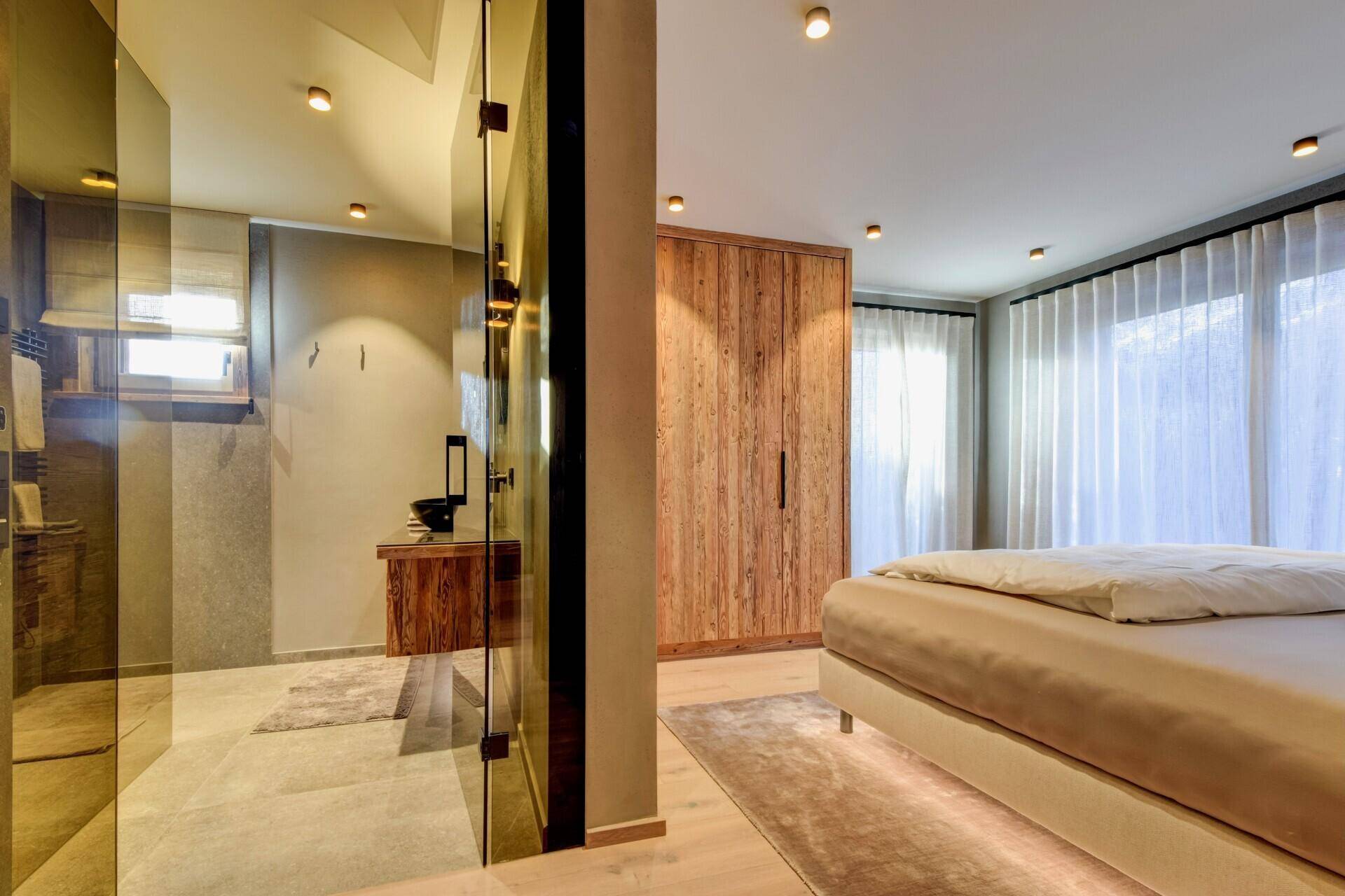 Schlafzimmer mit integriertem Badbereich, Holzwänden und großen Fenstern für viel Licht.
