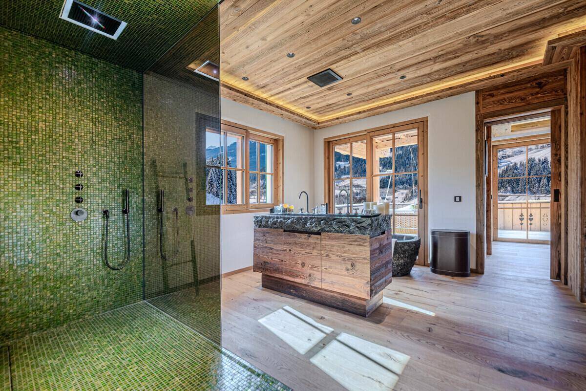Modernes Badezimmer mit großer begehbarer Dusche, Steinwaschtisch und Blick auf die Winterlandschaft.