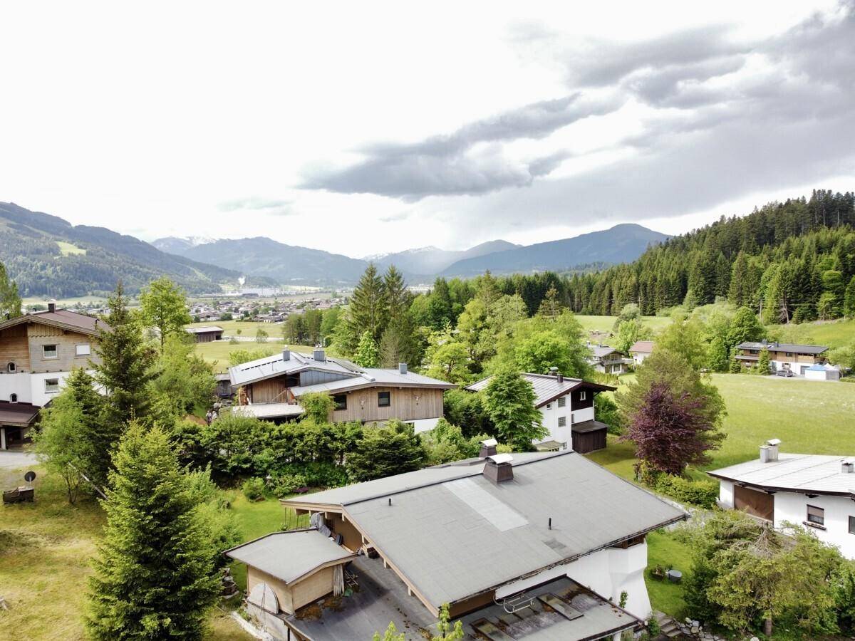Blick über eine ländliche Siedlung mit Häusern und grüner Umgebung, umgeben von Bergen.