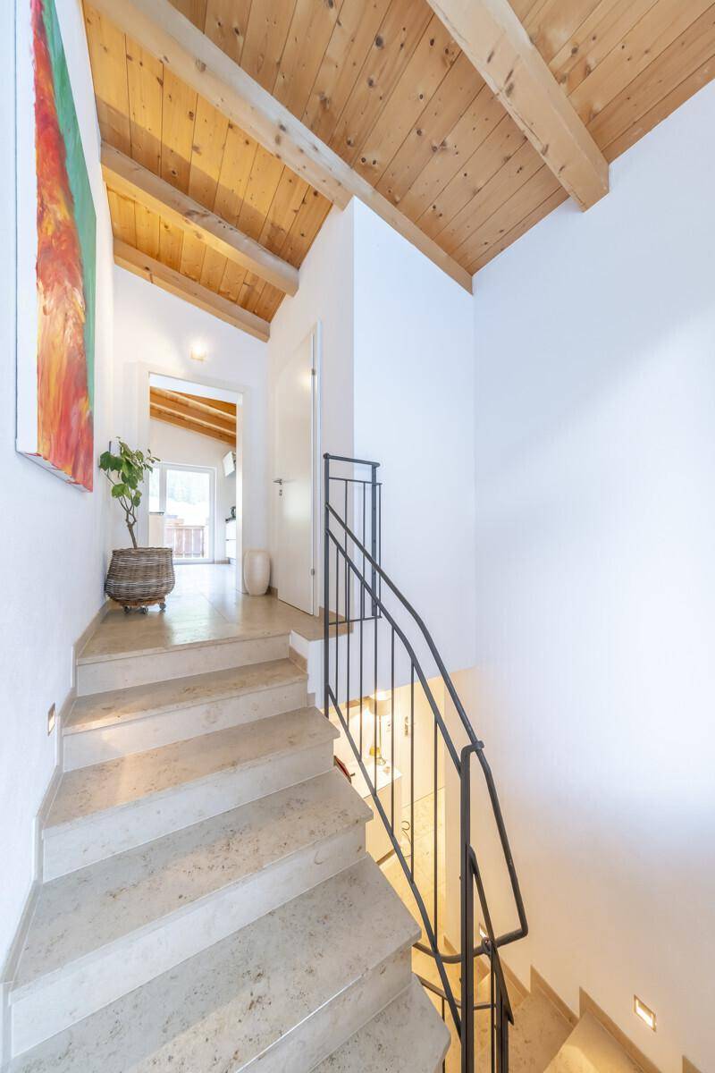 Heller Flur mit Steintreppe, schmiedeeisernem Geländer und Holzbalkendecke.