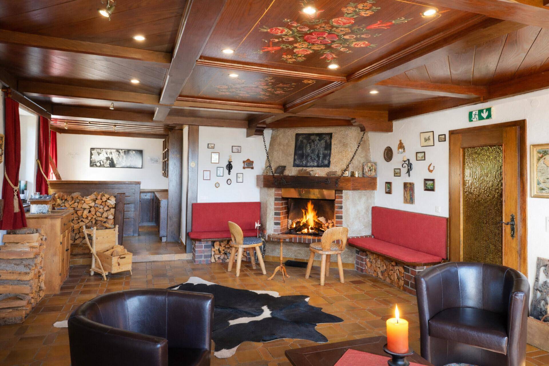 Rustikales Wohnzimmer mit offenem Kamin, Holzbalkendecke und traditionellen Sitzgelegenheiten für gemütliche Abende.