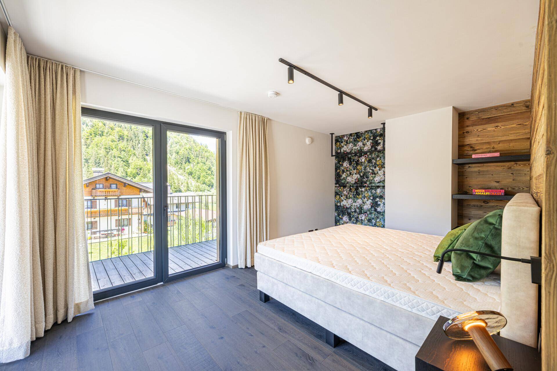 Helles Schlafzimmer mit Holzwand, Balkonzugang und Blick auf die grüne Umgebung.