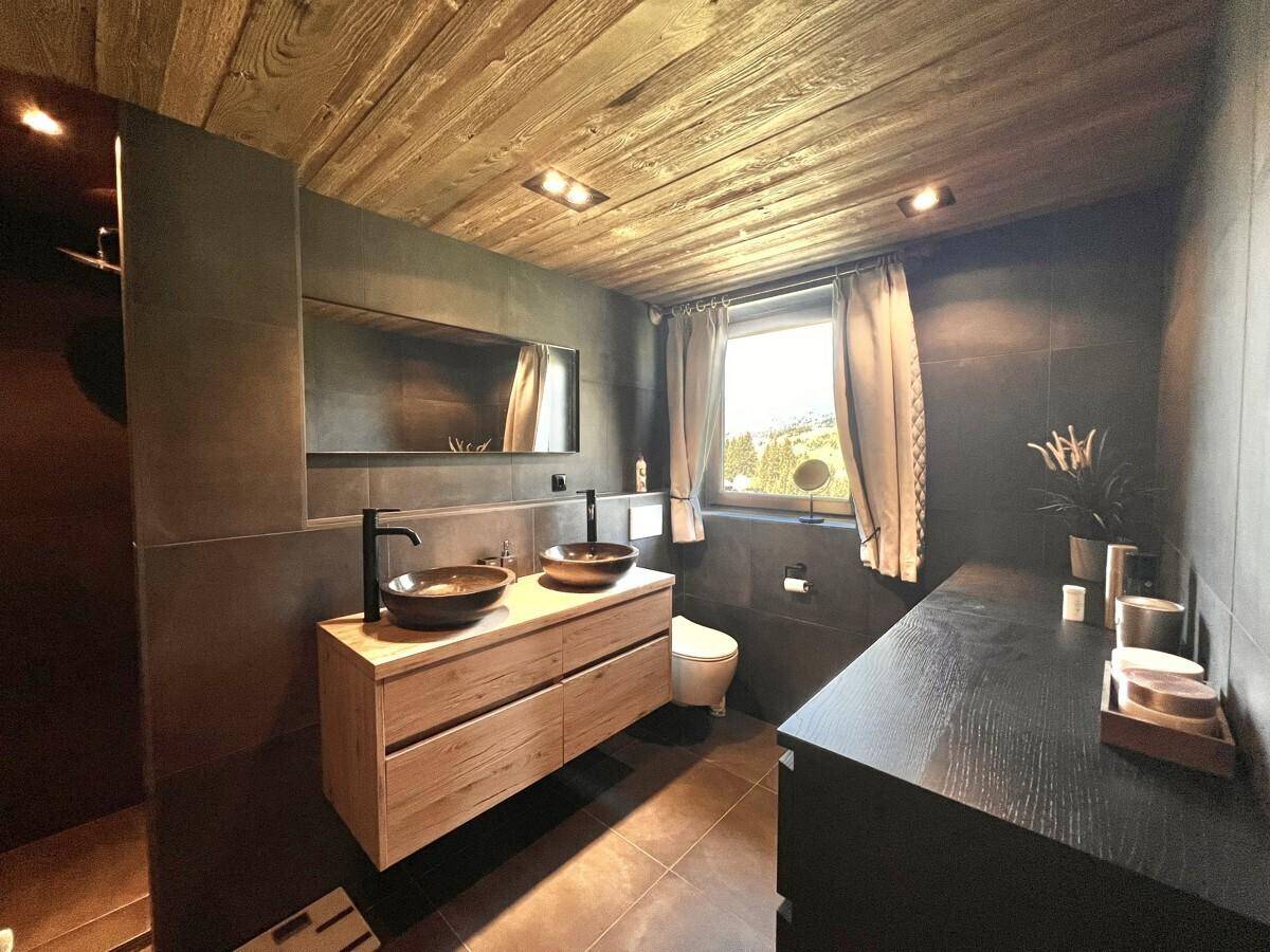 Modernes Badezimmer mit dunklen Fliesen, Holzwaschtisch und zwei Aufsatzwaschbecken.