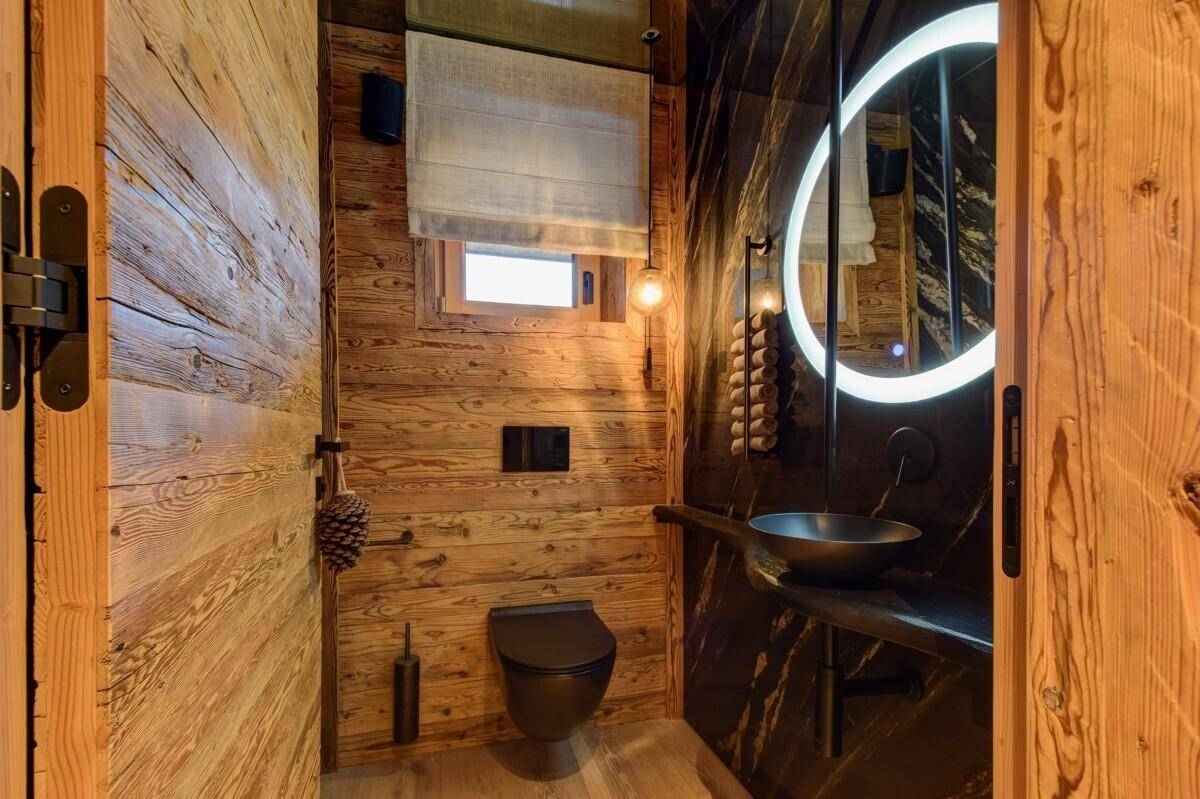 Modernes Gäste-WC mit Holzverkleidung, dunklem Waschbecken und beleuchtetem Spiegel.