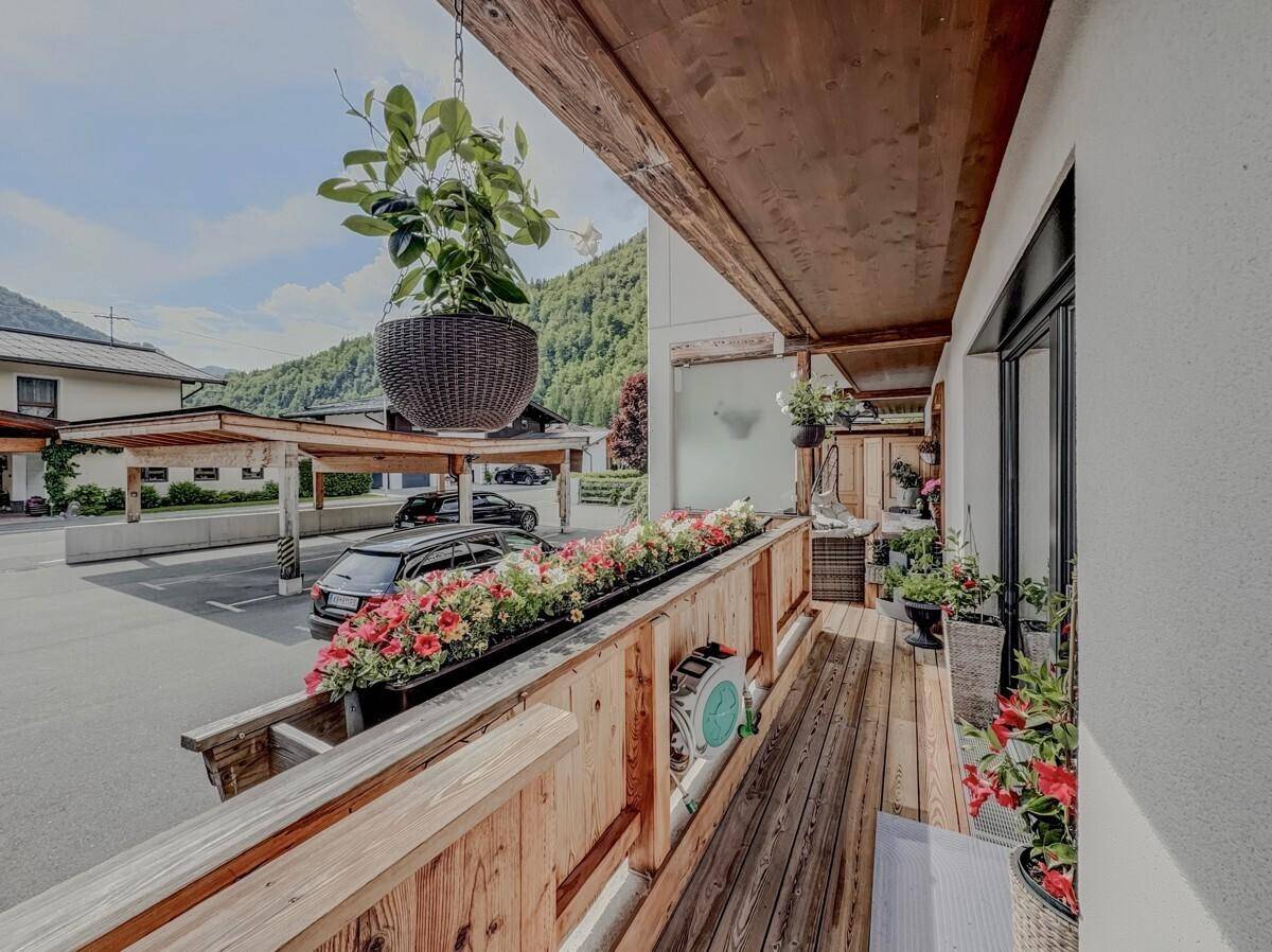 Balkon mit Blumenkästen und Blick auf den Parkplatz und die umliegenden Berge.