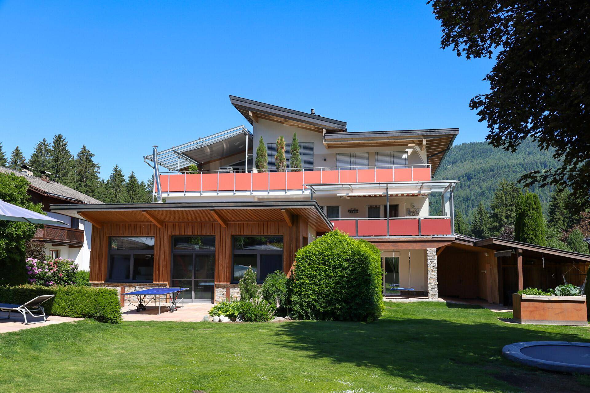 Weitläufiger Gartenbereich mit moderner Architektur, Terrasse und Tischtennisplatte im Freien unter blauem Himmel.