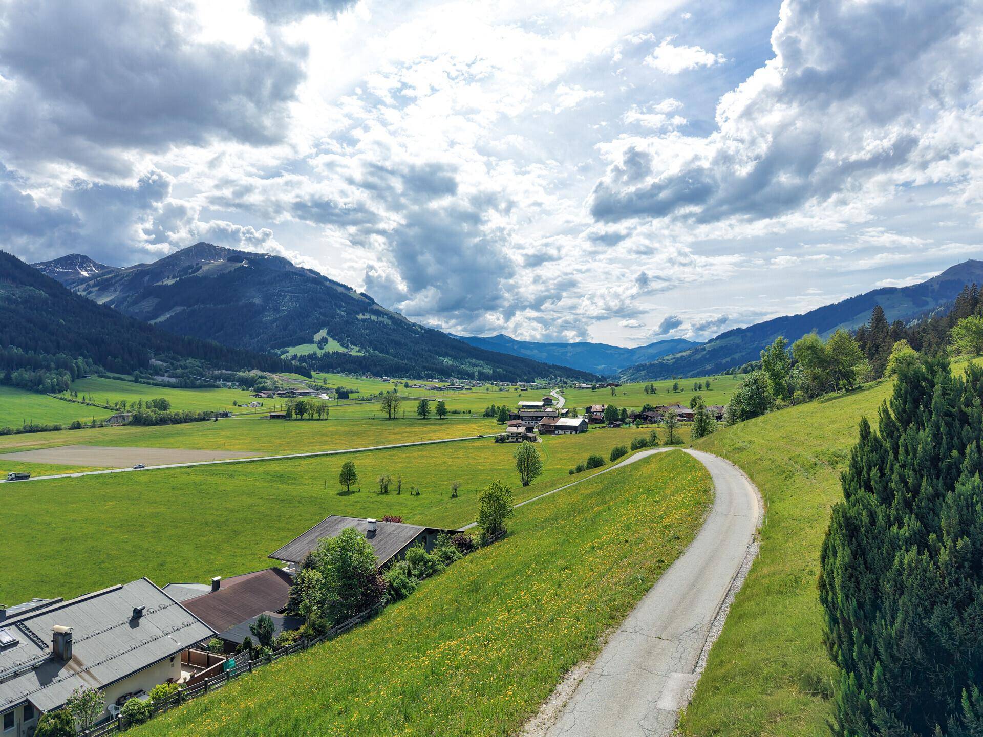 Weitläufige Landschaftsaufnahme eines grünen Tals mit verstreuten Häusern und majestätischen Bergen im Hintergrund.