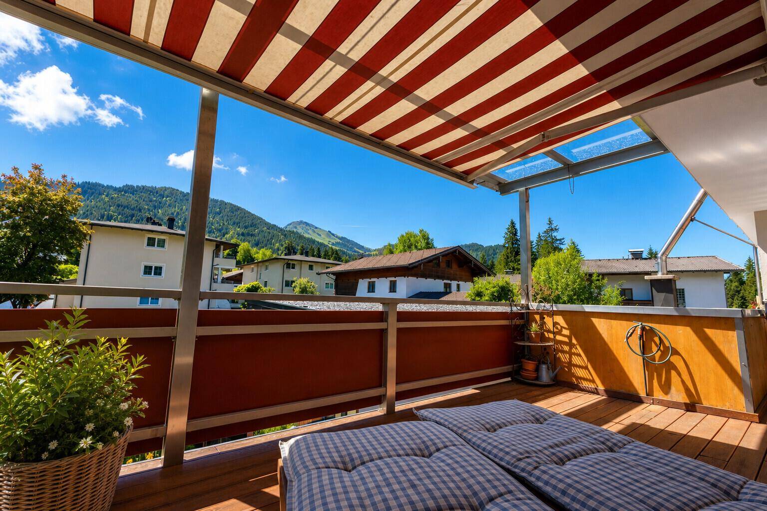 Sonniger Balkon mit Holzdeck, gestreifter Markise und Liegestühlen, bietet einen weiten Bergblick.