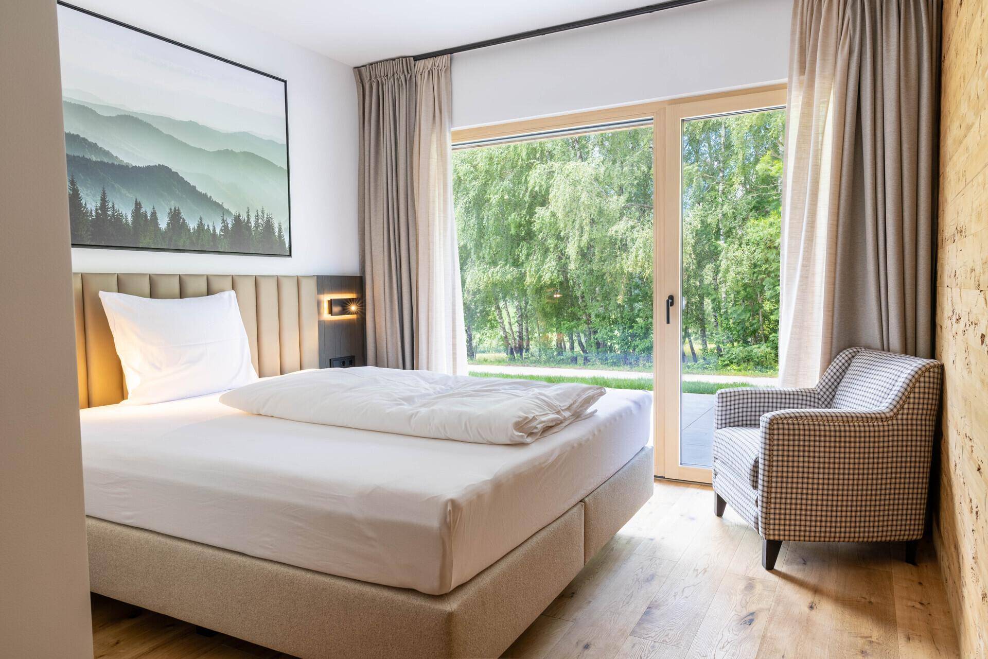 Helles Schlafzimmer mit Doppelbett, Holzboden und großem Fenster mit Waldblick.