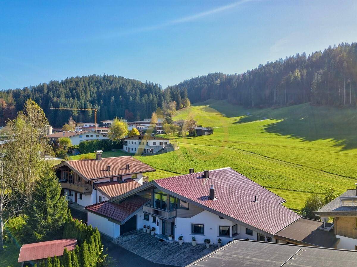 Luftaufnahme der Villa in einer grünen Hügellandschaft mit umliegenden Häusern.