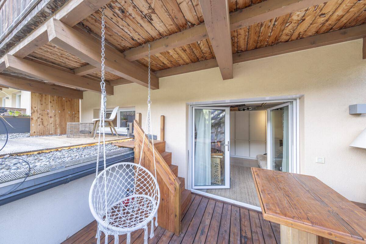 Überdachte Holzterrasse mit Hängesessel und direktem Zugang zu einem Innenraum.